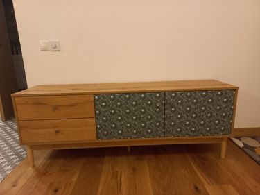 Собран деревянный шкаф с двумя ящиками и дверцами с узором. Установлены ножки, прикреплены ручки. Все элементы соединены, конструкция устойчива и готова к использованию.