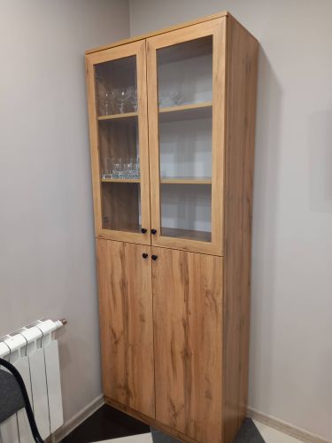 Собран шкаф с двумя секциями, стеклянными дверцами и деревянными полками. Установлены ручки, отрегулированы петли, проверена устойчивость. Готов к использованию и хранению вещей.