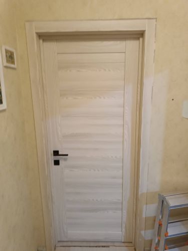 Установлена деревянная створка, закреплённая в проёме, с врезанным замком и ручкой. Коробка выровнена, наличники прикреплены, зазоры устранены, обеспечена плавная работа.