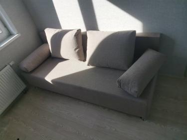 Собран диван: установлены подлокотники, прикреплены спинка и ножки, размещены подушки. Компактно и аккуратно завершён монтаж.