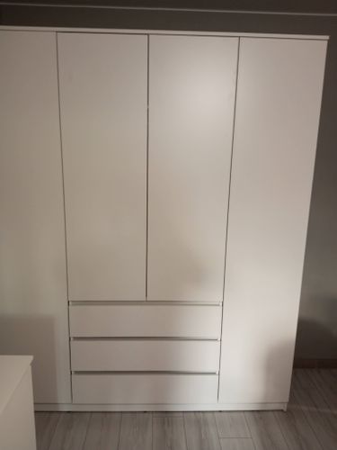 Собран белый шкаф с тремя дверцами и тремя выдвижными ящиками. Все элементы установлены ровно, без зазоров. Конструкция устойчива, гармонично вписывается в интерьер комнаты.