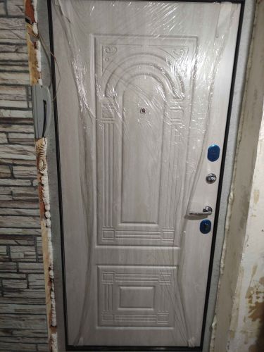 Установлена новая дверь с замком и ручкой, закреплена в проеме, зазоры заделаны монтажной пеной, защитная пленка оставлена на поверхности для сохранности.