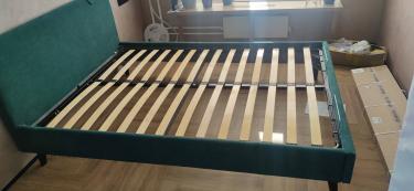 Собрана двуспальная кровать: установлены ножки, закреплены боковины, уложены ламели, зафиксировано изголовье. Все элементы соединены, конструкция устойчива, готова к использованию.