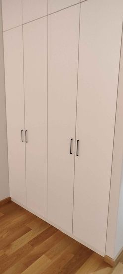 Изображение демонстрирует белый шкаф с четырьмя дверцами и черными ручками. На переднем плане виден деревянный пол.