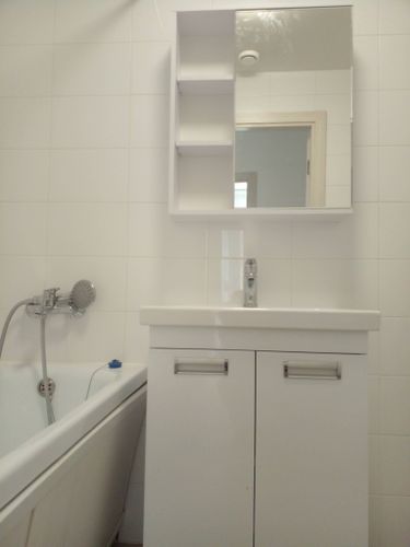 Изображение ванной комнаты с белым шкафчиком, зеркалом и ванной. Установлен новый смеситель, подключены трубы, проверена герметичность соединений, обеспечена функциональность.