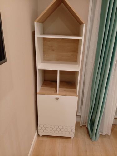 Собран новый угловой стеллаж с полками и шкафчиком, установлен в комнате. Конструкция выполнена из светлого дерева и белых панелей, гармонично вписывается в интерьер.