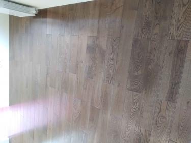 На полу уложены панели с текстурой дерева, ровно и аккуратно, без зазоров. Поверхность гладкая, с естественным рисунком, придающим комнате уют и стильный вид.