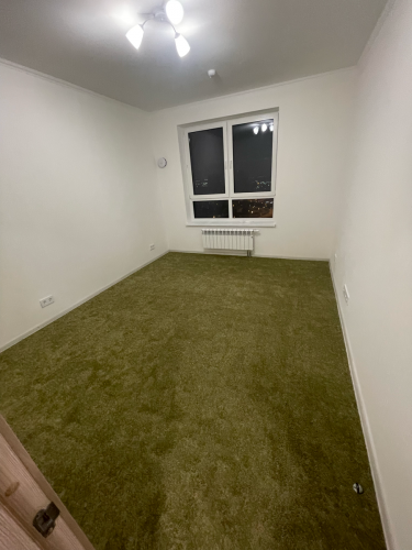 В комнате на полу уложено ковровое покрытие, тщательно подогнанное по периметру, создающее уютную и гармоничную атмосферу. Полностью завершенный процесс без видимых швов.