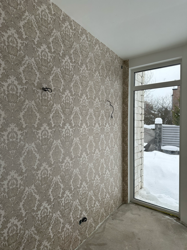 Стены покрыты декоративными обоями с узором, тщательно выровнены и аккуратно оформлены. Присутствуют вырезы для розеток и выключателей, работа выполнена качественно.