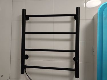 На стене закреплён чёрный полотенцесушитель, установленный надёжно и ровно. Проведены монтажные работы, подключение к электросети выполнено аккуратно.