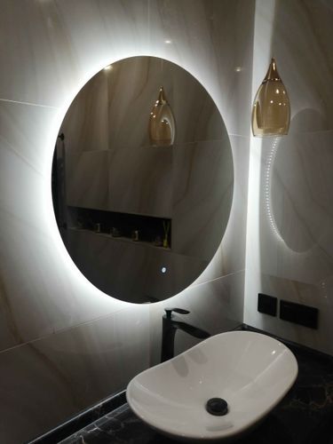 Изображен круглый зеркальный шкаф с подсветкой, надежно закрепленный на стене ванной комнаты. Установлены крепления, обеспечивающие устойчивость и безопасность конструкции.