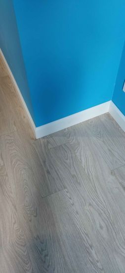 Установлен белый плинтус вдоль стены, создающий аккуратный переход между полом и стеной. Завершённый монтаж подчёркивает чистоту линий и гармонию интерьера.