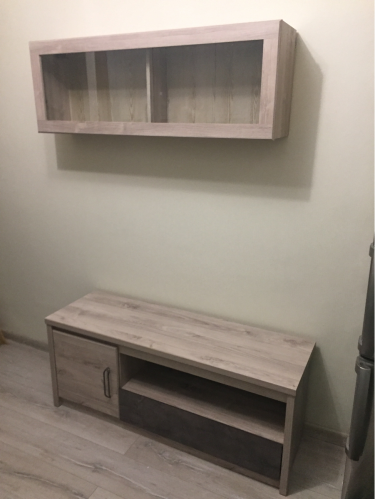 На стене закреплена деревянная полка с двумя секциями. Установлена ровно, надежно, без видимых крепежей. Под ней расположен шкаф с дверцей и открытой нишей.