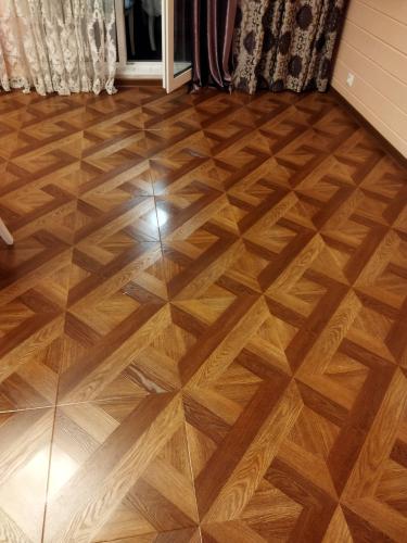 На изображении завершена работа по укладке ламината. Пол ровный, с геометрическим рисунком, создающим эффект паркета. Цвет покрытия тёплый, гармонирует с интерьером помещения.