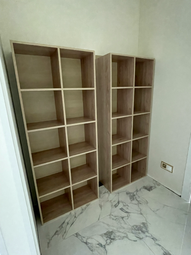 Собраны два деревянных стеллажа с девятью секциями каждый, установлены на полу с мраморным покрытием, выровнены по стене, обеспечена устойчивость и надежность конструкции.