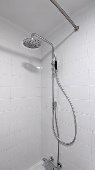 Изображение демонстрирует установленный душевой комплект с круглой лейкой и гибким шлангом на белой плитке. Все элементы надежно закреплены, система готова к использованию.