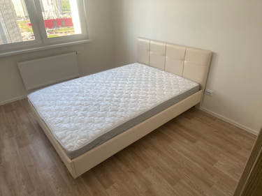 Собрана двуспальная кровать: установлены каркас, изголовье, матрас. Все элементы надежно закреплены, конструкция устойчива. Работа завершена, мебель готова к использованию в интерьере.