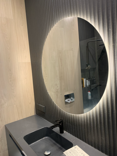 Завершено крепление круглого зеркала с подсветкой над раковиной в ванной комнате. Установлено на стену с декоративной отделкой, обеспечена надежная фиксация и подключение освещения.