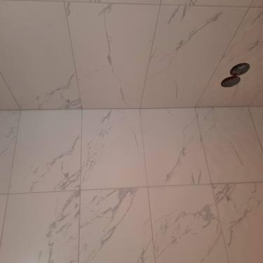 На стену ровно уложены плитки с мраморным узором, швы аккуратно заделаны, поверхность гладкая, без дефектов, отверстия под коммуникации вырезаны точно.