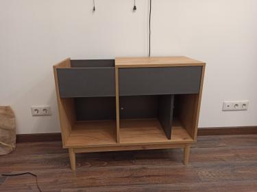 Собрана мебель: установлены ножки, закреплены боковые панели, прикреплены полки, добавлены фасады. Все элементы соединены, конструкция устойчива и готова к использованию.