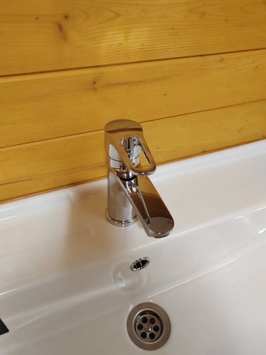 Завершена установка нового крана, обеспечивающего надежное перекрытие потока воды. Устройство блестит на фоне деревянной стены, гармонично вписываясь в интерьер.