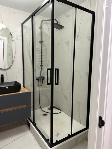 Установлена стеклянная конструкция с черными рамами и дверями, закреплён поддон, подключены смеситель и душевой шланг, произведена герметизация швов для предотвращения протечек.