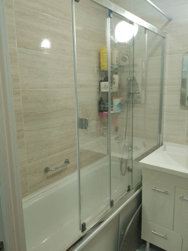 Установлена акриловая ванна, закреплены стеклянные шторки, подключены смеситель и душ, выполнена герметизация швов, добавлены полочки для аксессуаров, завершена отделка плиткой.