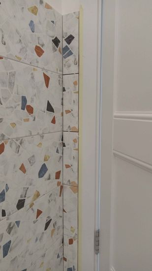 Уложена керамическая плитка на стены, швы аккуратно заделаны, поверхность ровная, использованы разноцветные элементы для создания мозаичного узора, примыкания обработаны.