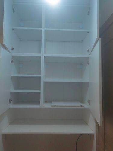 Установлены белоснежные шкафы с полками, закреплены петли, дверцы ровно навешены, обеспечена прочная фиксация, внутренние секции выровнены, завершена сборка, обеспечена функциональность.