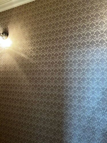 На стене аккуратно наклеены обои с изящным узором. Поверхность ровная, без видимых стыков и пузырей. Декор придает комнате элегантный и завершенный вид.