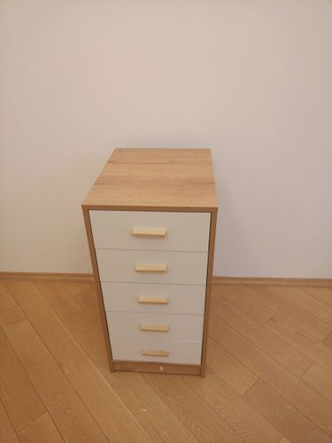 Собран деревянный шкаф с пятью ящиками. Установлены ручки, выровнены фасады. Конструкция устойчива, все детали надежно закреплены. Завершена установка на деревянный пол.