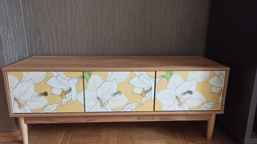 Собран деревянный шкаф с тремя дверцами, украшенными цветочным рисунком. Установлены ножки, дверные ручки закреплены, конструкция устойчива, готова к использованию.