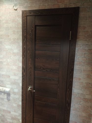 Установлена новая деревянная дверь, закреплены петли, врезана ручка, отрегулировано полотно, проверена плавность открывания, завершена отделка наличниками, обеспечена надежная фиксация.