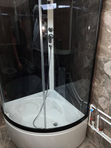 Установлена новая душевая кабина с полукруглым поддоном и стеклянными дверцами. Подключены водопроводные трубы и слив. Завершена отделка стен плиткой, обеспечена герметичность.