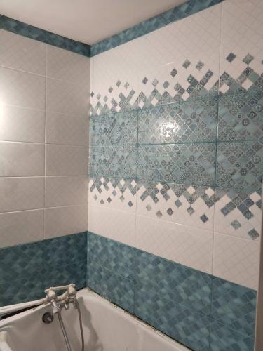 Ванная комната облицована керамической плиткой с узором. Поверхности стен покрыты белыми и голубыми элементами, создающими декоративный орнамент. Углы и стыки аккуратно оформлены.