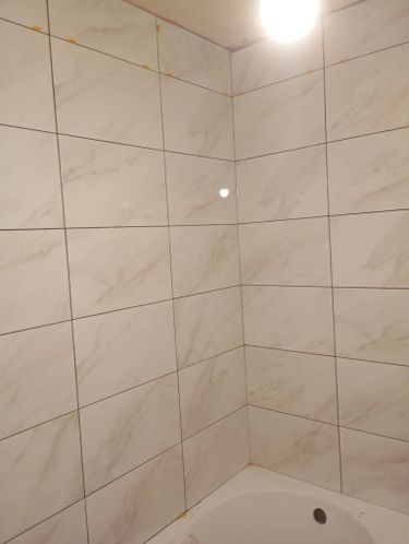 На стенах ванной комнаты ровно уложен керамогранит с мраморным узором. Швы тщательно заполнены, поверхность гладкая и аккуратная. Углы и стыки обработаны, создавая завершенный вид.