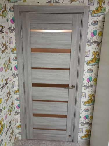 Установлена новая межкомнатная дверь с петлями, замком и ручкой. Полотно ровно закреплено в проеме, обеспечивая плавное открывание и закрывание. Монтаж завершен, все элементы на месте.