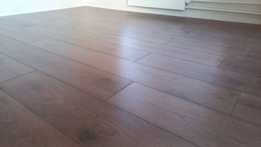 На ровное основание уложено напольное покрытие из ламината с аккуратными стыками и ровными швами, создающими гладкую и эстетичную поверхность.