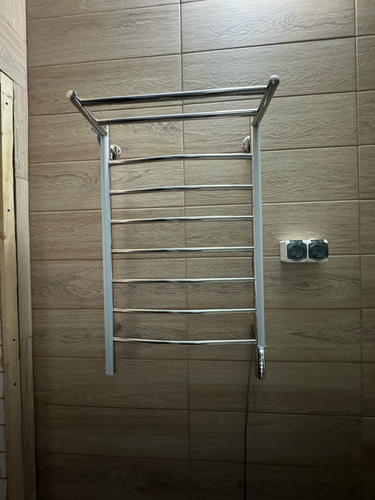 На стене закреплен электрический прибор для сушки полотенец. Подключение выполнено к электросети, обеспечена надежная фиксация и безопасная эксплуатация устройства.