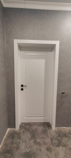 На белой двери установлен новый замок. Проведены работы по вырезанию отверстия, монтажу механизма и ручки. Все элементы аккуратно закреплены, обеспечивая надежное закрытие.