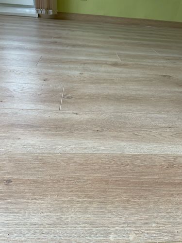 На ровное основание уложен ламинат, образуя гладкую поверхность. Панели плотно соединены, создавая единое покрытие без зазоров. Завершён монтаж плинтусов вдоль стен.