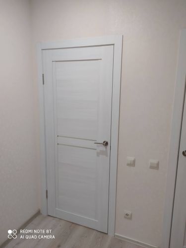 Установлена новая белая дверь с ручкой и петлями, ровно вмонтирована в проем. Завершена отделка откосов и наличников, обеспечена плавная работа механизма.