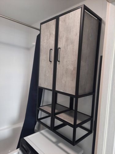 Изображение демонстрирует завершённую установку шкафа в ванной комнате. Шкаф закреплён на стене над стиральной машиной, выполнен в современном стиле с металлическим каркасом и деревянными дверцами.