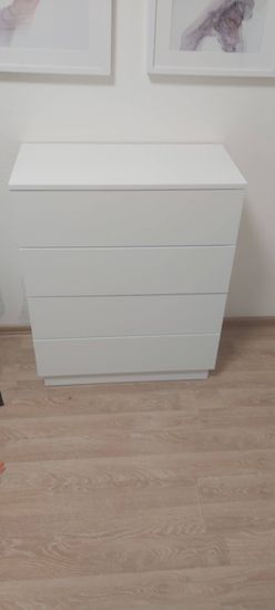Собран белый комод с четырьмя ящиками, установлены все детали, обеспечена устойчивость конструкции, проверена функциональность выдвижных элементов, выполнена окончательная сборка.