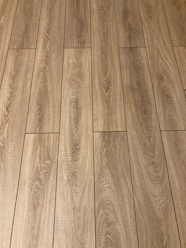 На ровное основание уложено напольное покрытие из ламината. Плашки аккуратно соединены, образуя гладкую поверхность с текстурой дерева. Завершена работа по созданию стильного интерьера.