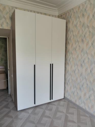 Собран шкаф с тремя дверцами, установлен в углу комнаты. Белая поверхность, черные ручки. Ровно выровнены, надежно закреплены детали. Завершено оформление интерьера.