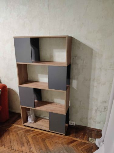 Собран современный стеллаж с деревянными полками и серыми вставками, установлен на деревянный пол у стены, готов к использованию.