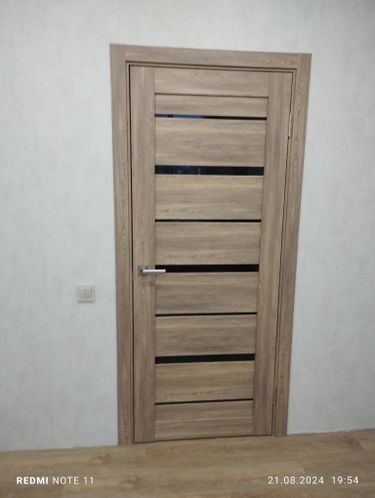 Установлена новая дверь с деревянной текстурой, закреплена фурнитура, отрегулированы петли, добавлена ручка, выполнена отделка проема, обеспечена плавная работа конструкции.