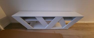 Собран белый шкаф с диагональными полками, установлен на деревянный пол у стены. Компактная конструкция завершена, элементы надежно соединены, обеспечивая устойчивость и функциональность.