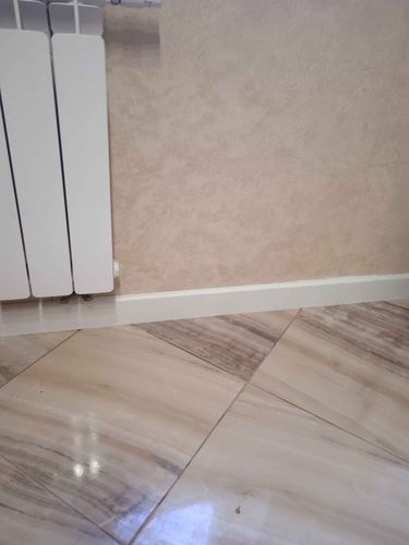 Установлен новый плинтус вдоль стены, аккуратно закреплённый на стыке с полом, обеспечивая завершённый вид и плавный переход между поверхностями.